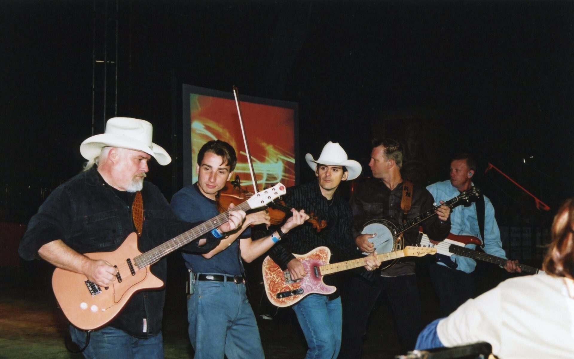 A band performing with guitars, a banjo, and a fiddle on stage.